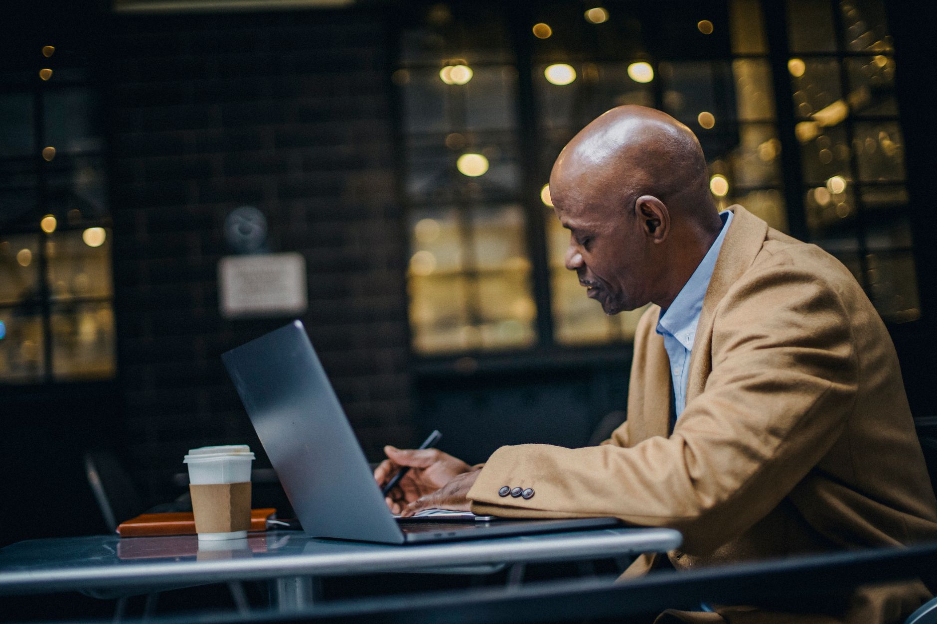 Side view of ethnic entrepreneur working near netbook and disposable glass of coffee at cafeteria table