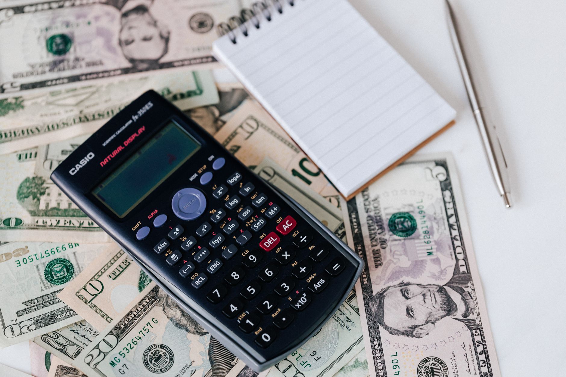 Calculator and notepad arranged over US dollar bills
