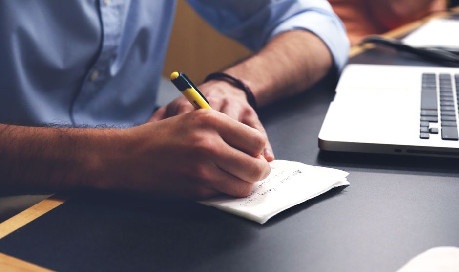A person checks notes beside a laptop before writing a response.