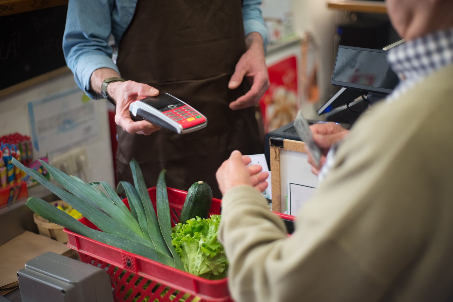 A cashier scanning items rapidly at a checkout while a customer waits with a trolley