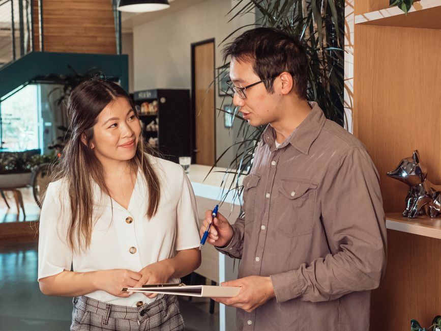 Two colleagues discuss work across a desk.
