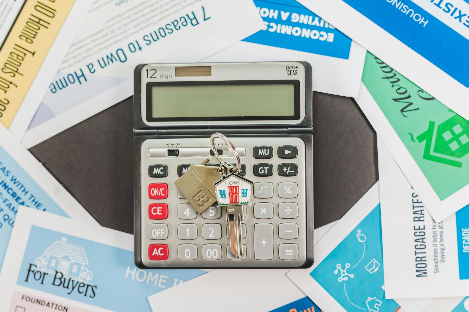 A person sitting at a kitchen table with a notebook, a calculator and a stack of household bills spread out in the morning light