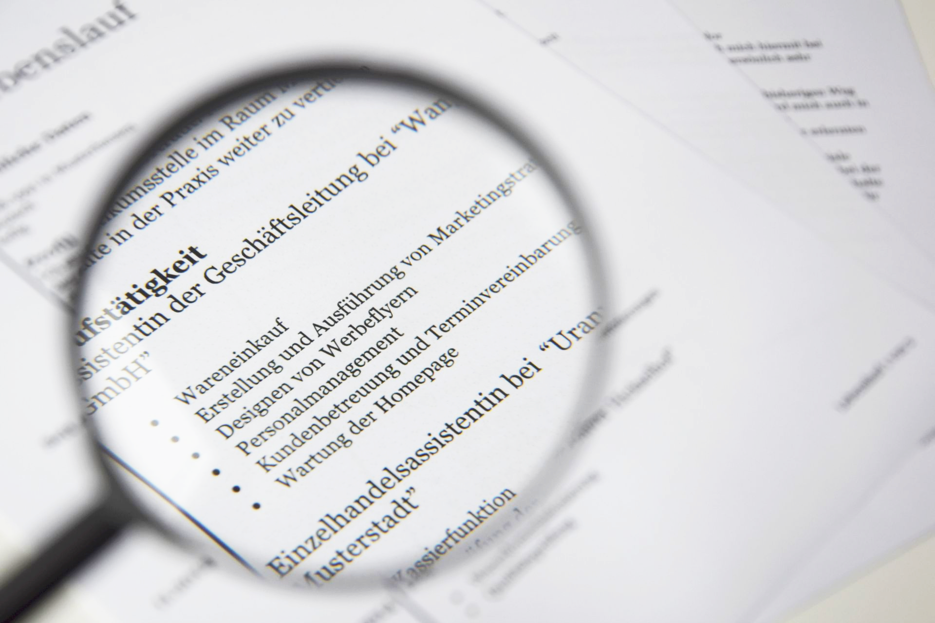A magnifying glass held over a printed résumé, enlarging a bulleted list of job duties under a work-experience heading