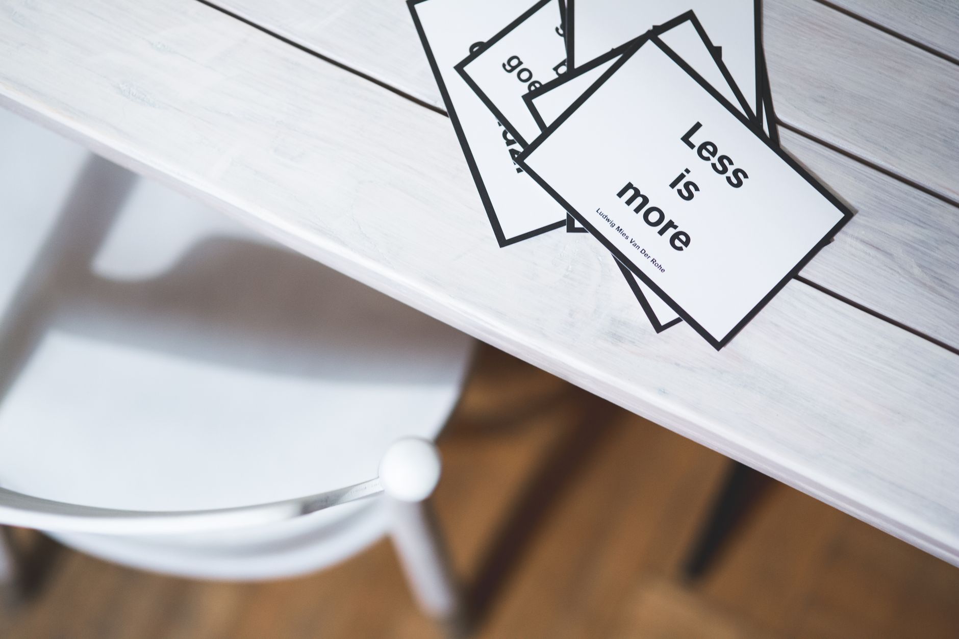 Design quote cards fanned out on a wooden table, the top card reading Less is more, attributed to Ludwig Mies van der Rohe