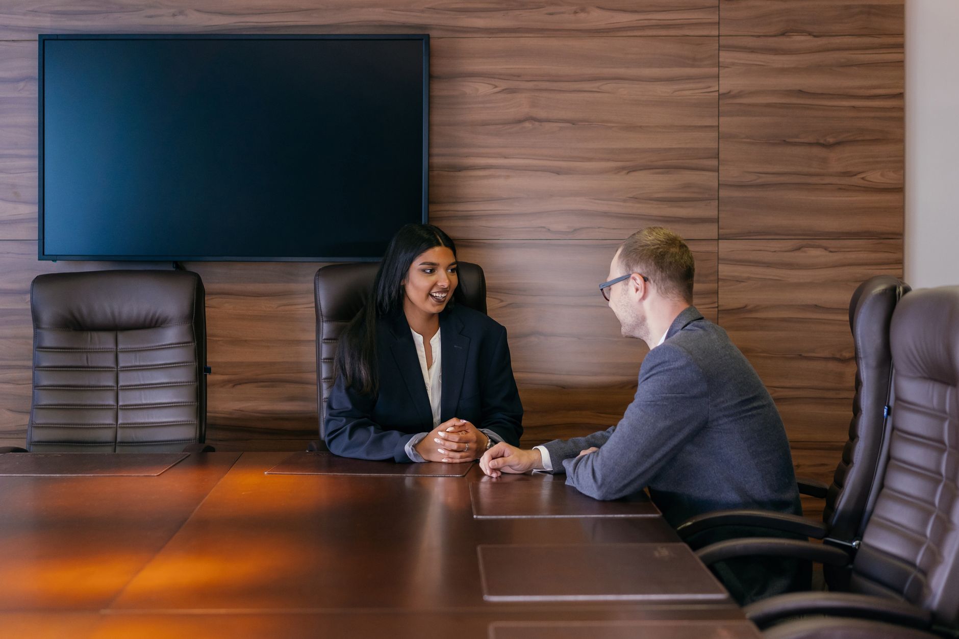 Two people sitting across a table during a job interview, one speaking while the other listens and takes notes