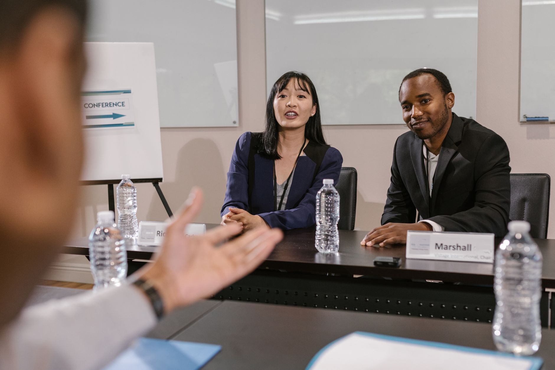A candidate speaking during an interview while an interviewer listens and takes notes across the table