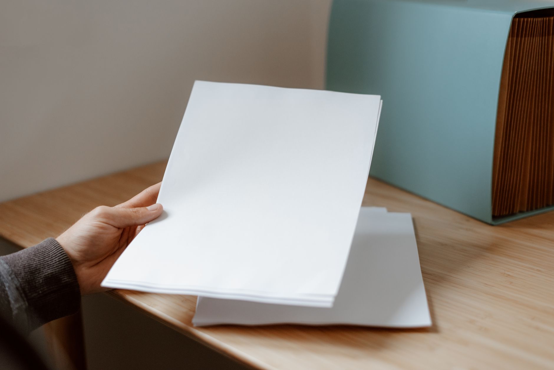 Crop anonymous person demonstrating empty sheet of paper against wooden table with folder for documents