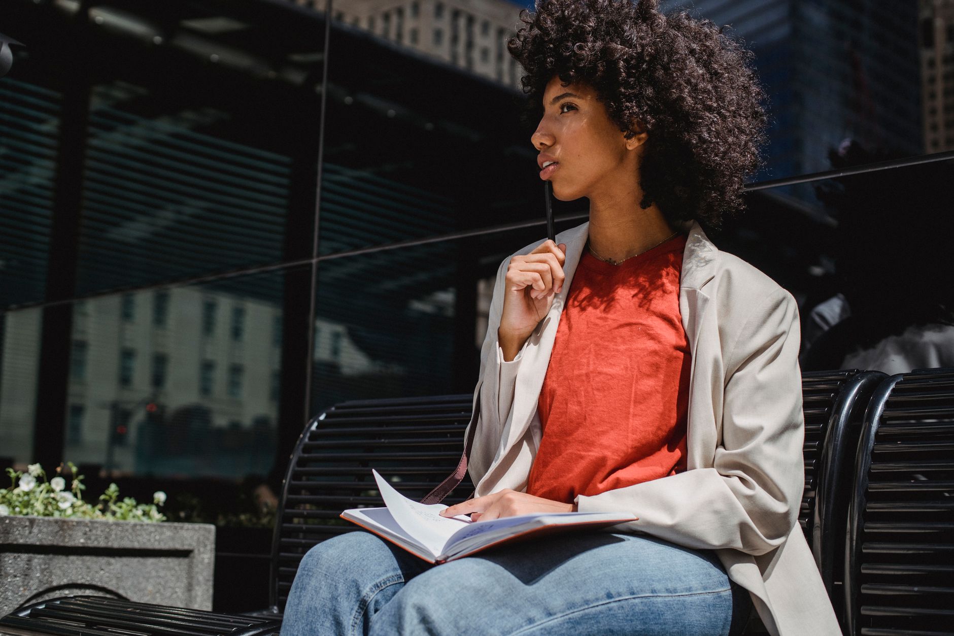 Woman sits outdoors on a bench, writing in a notebook in a city environment.