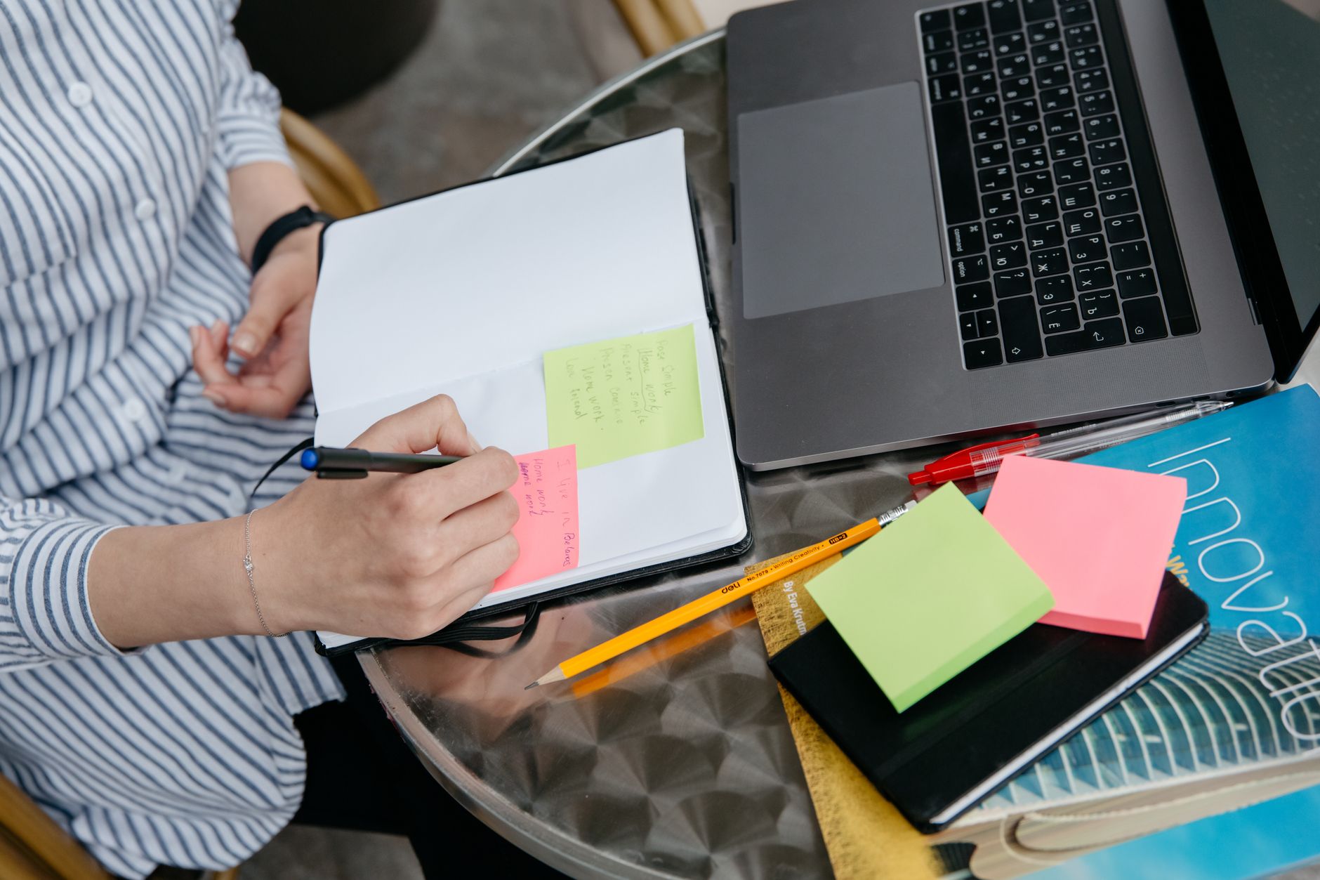 Person writing in a planning notebook beside a laptop and sticky notes