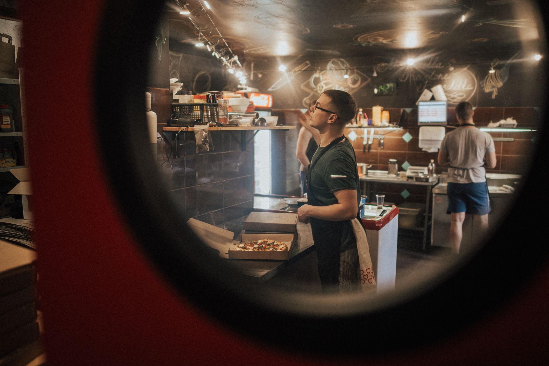 Customers waiting in a queue inside a fast casual restaurant while staff work behind a glass service counter