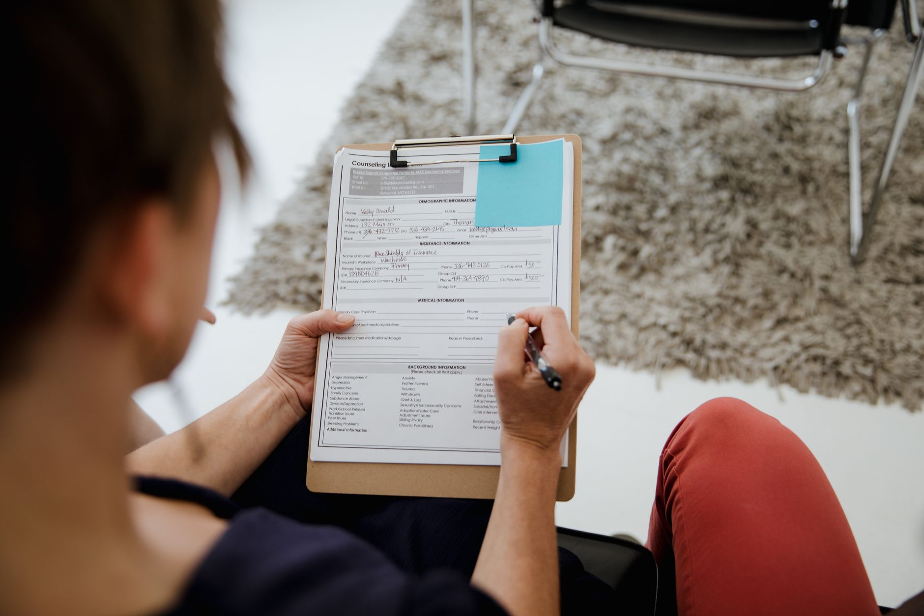 Two interviewers seated at a table with printed forms in front of them, one writing while the other listens to a candidate