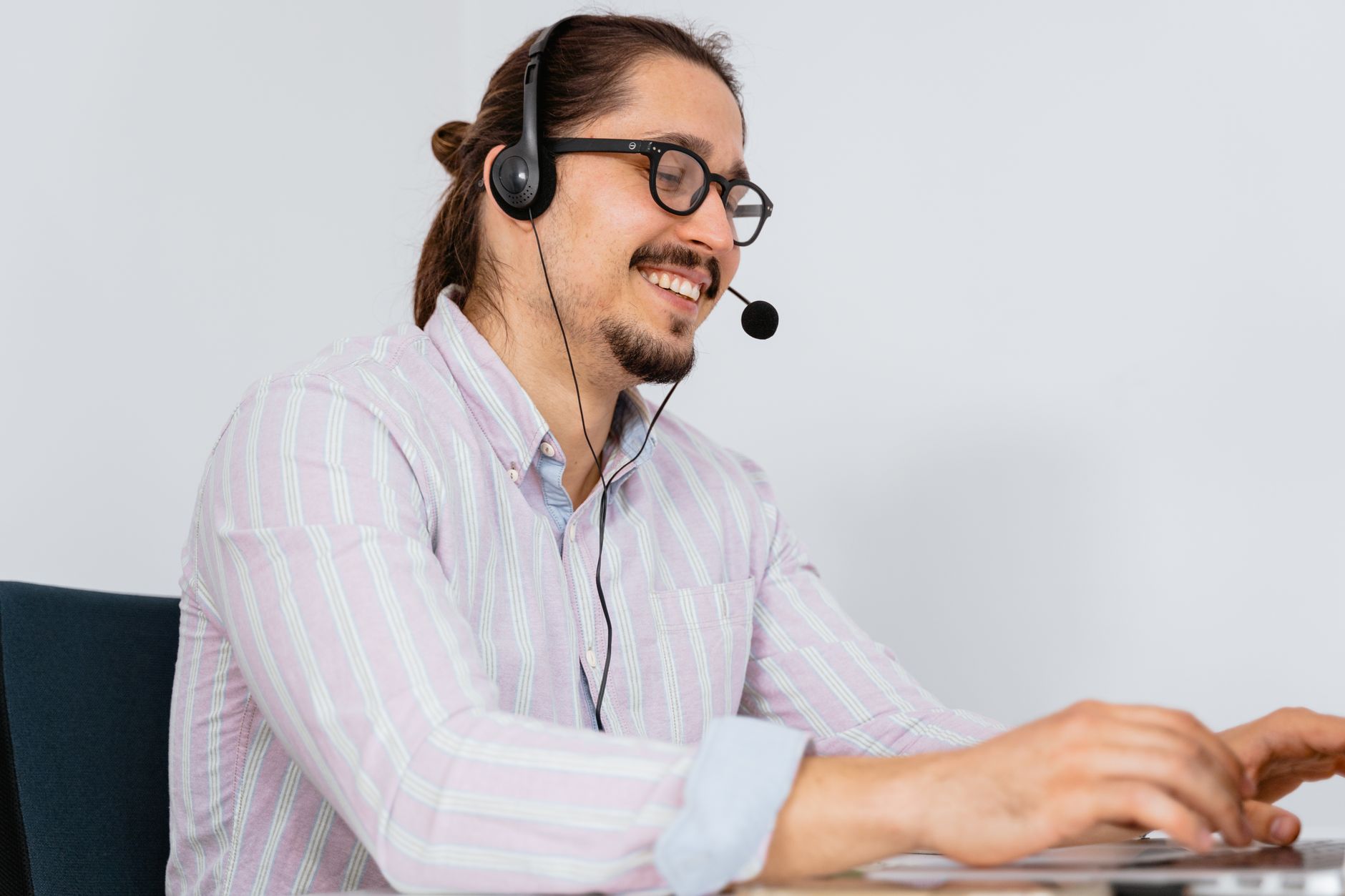 A support agent at a desk with a headset, mid-call, hand resting on a notepad rather than the keyboard