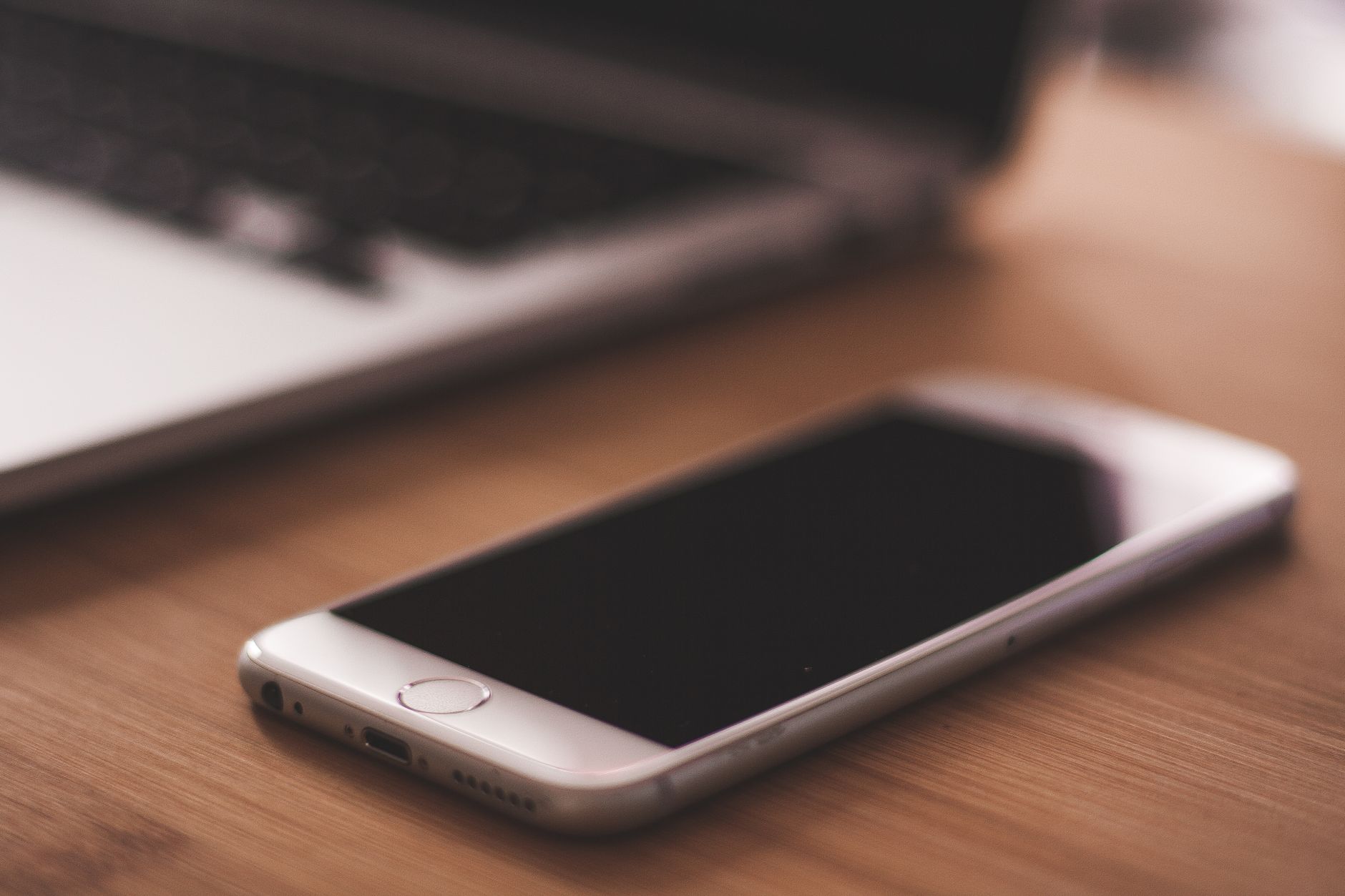 Smartphone resting on a wooden desk beside a laptop