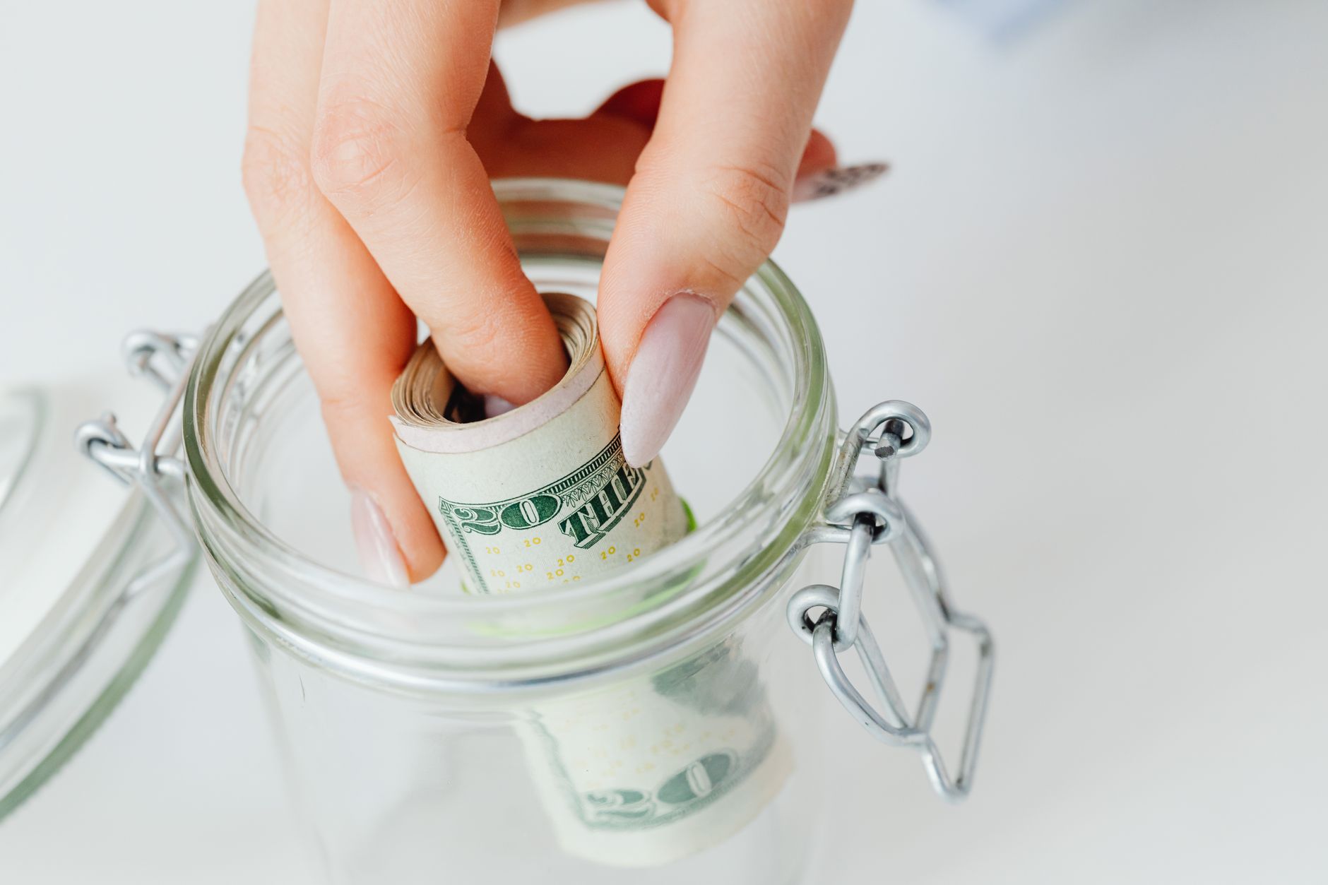 A hand placing rolled dollar bills into a glass savings jar