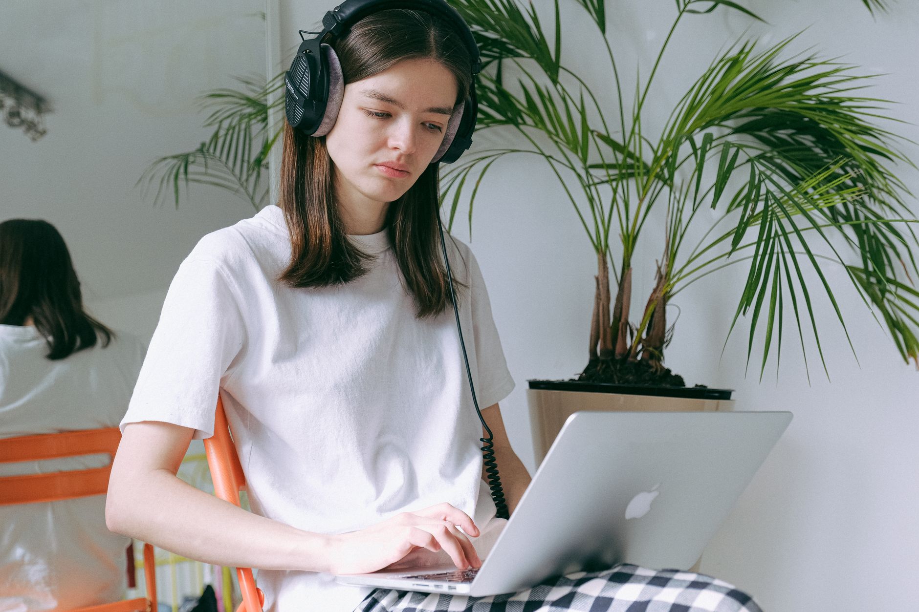 A person working at a desk with over-ear headphones on, laptop open, notebook and pen beside them
