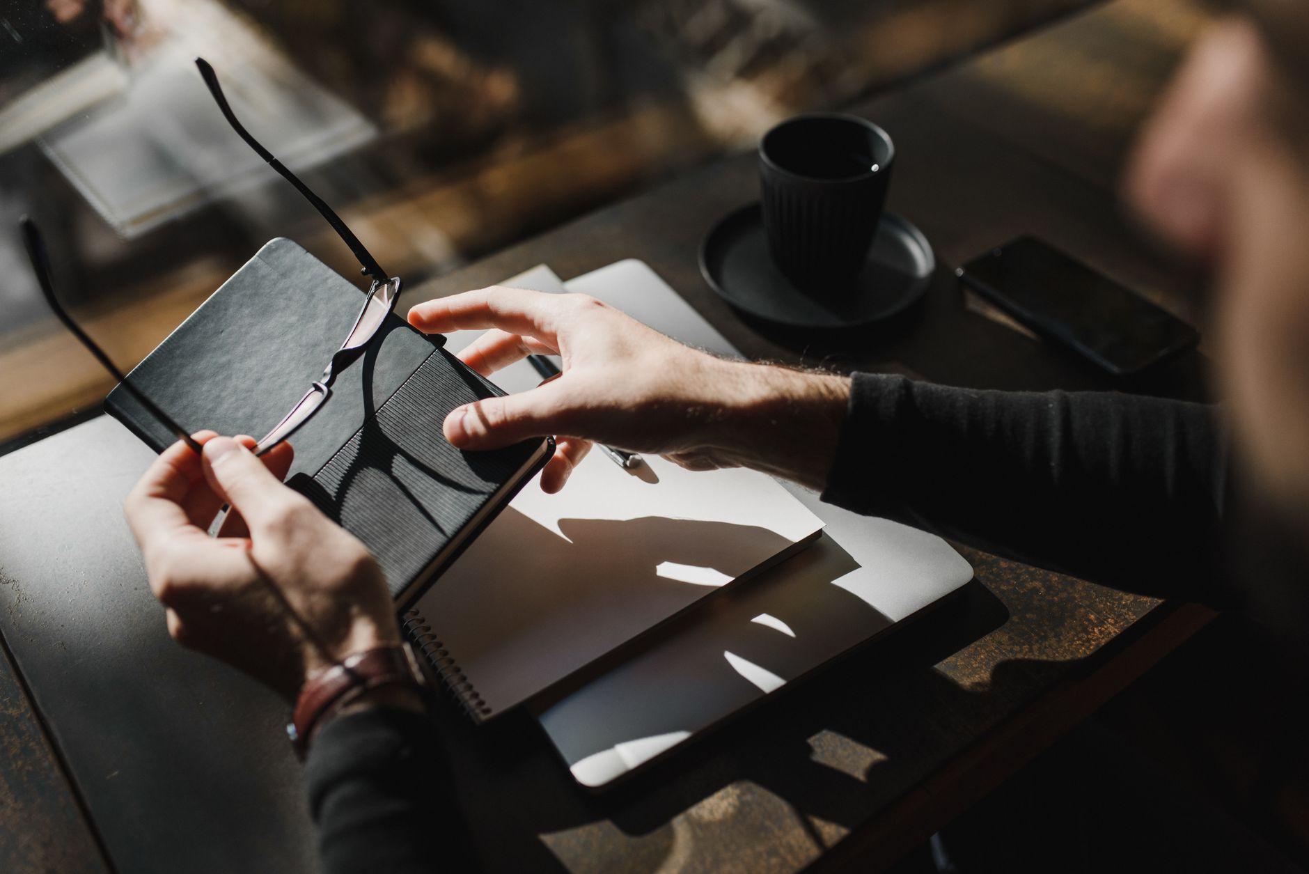Top view of hands holding eyeglasses and notebook on a desk with sunlight