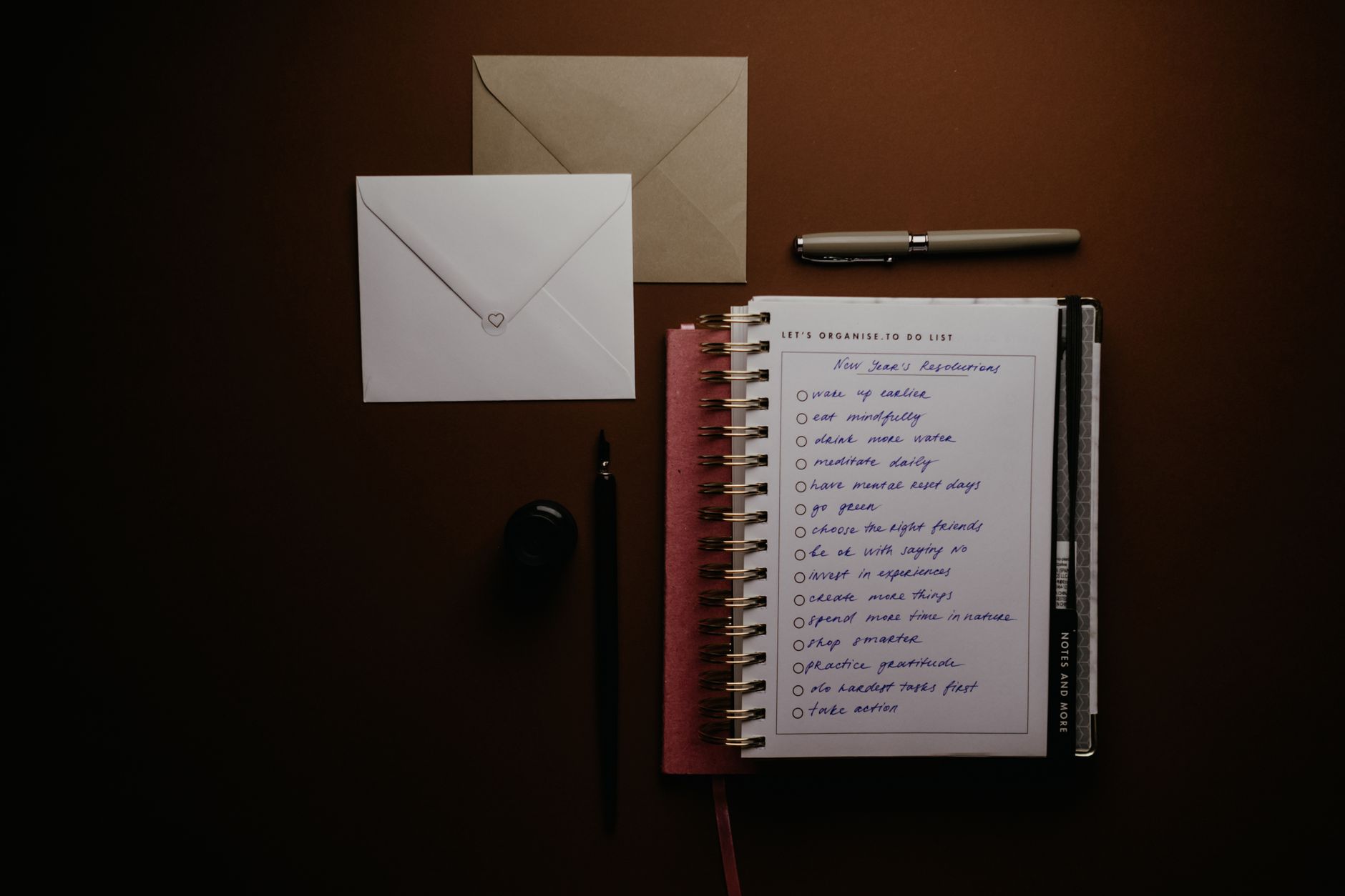 A hand writing a short list in a notebook with a pen, one item already checked off