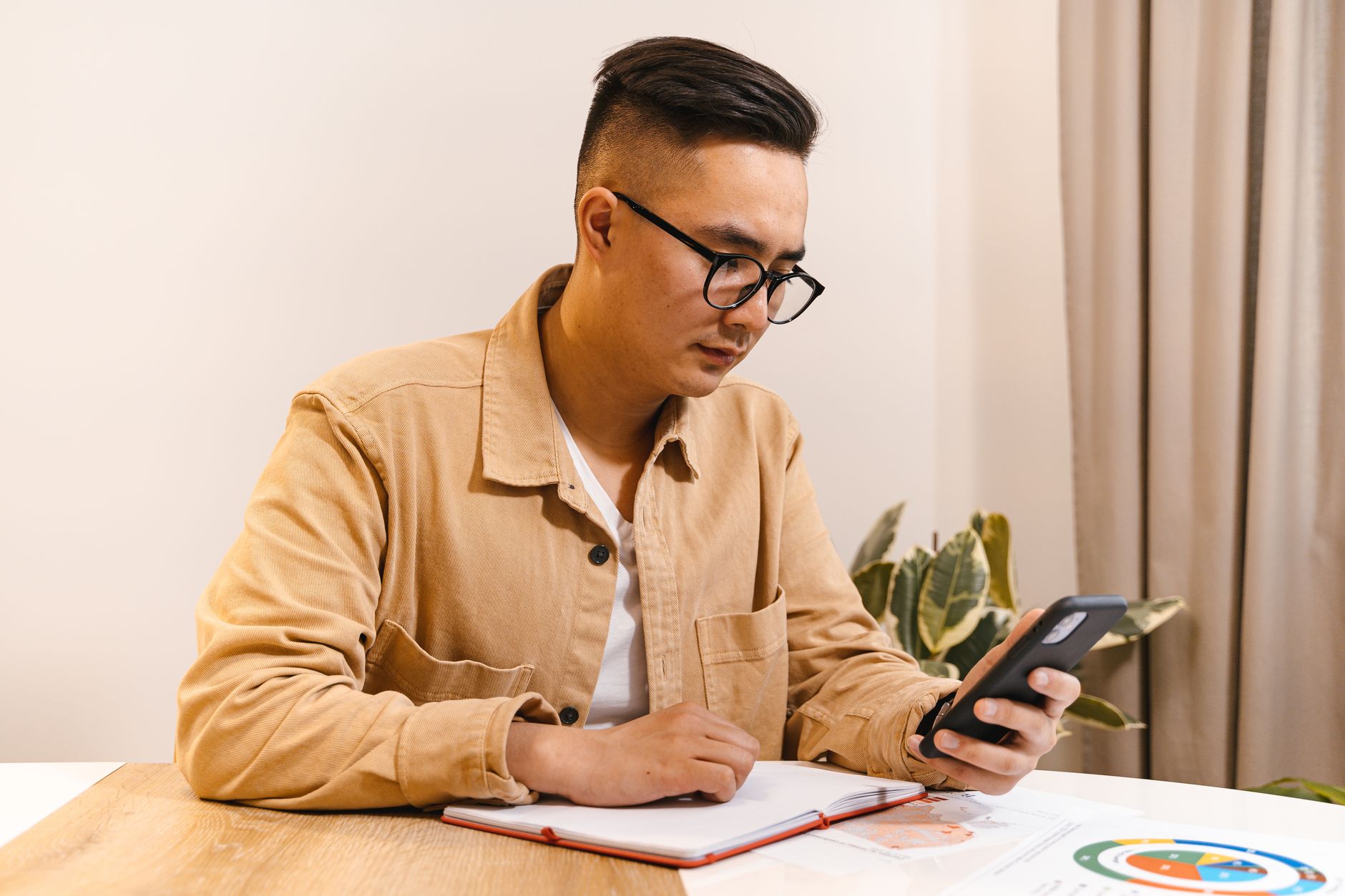 A single open notebook on a bare wooden desk with one line written on the page and a phone lying screen-down far out of reach at the edge of the room