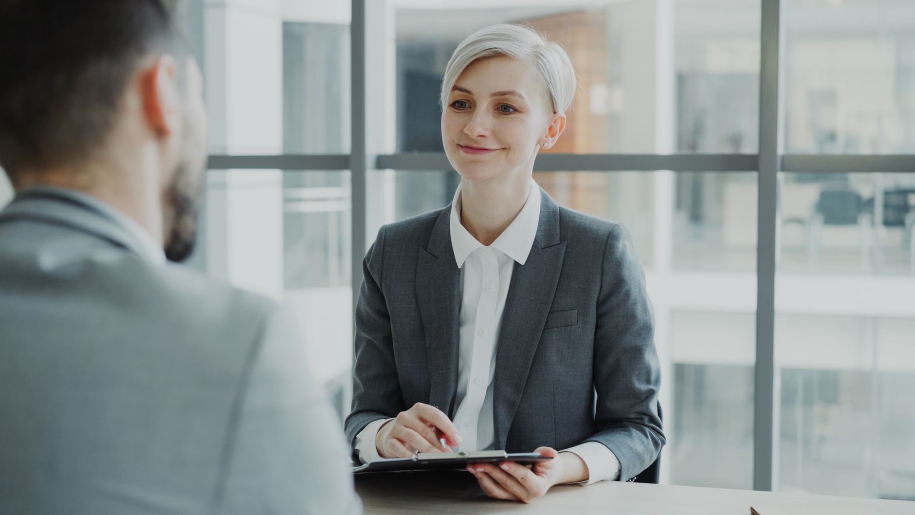 Two people talk across a small table in a quiet meeting room, one taking handwritten notes, the conversation clearly serious.