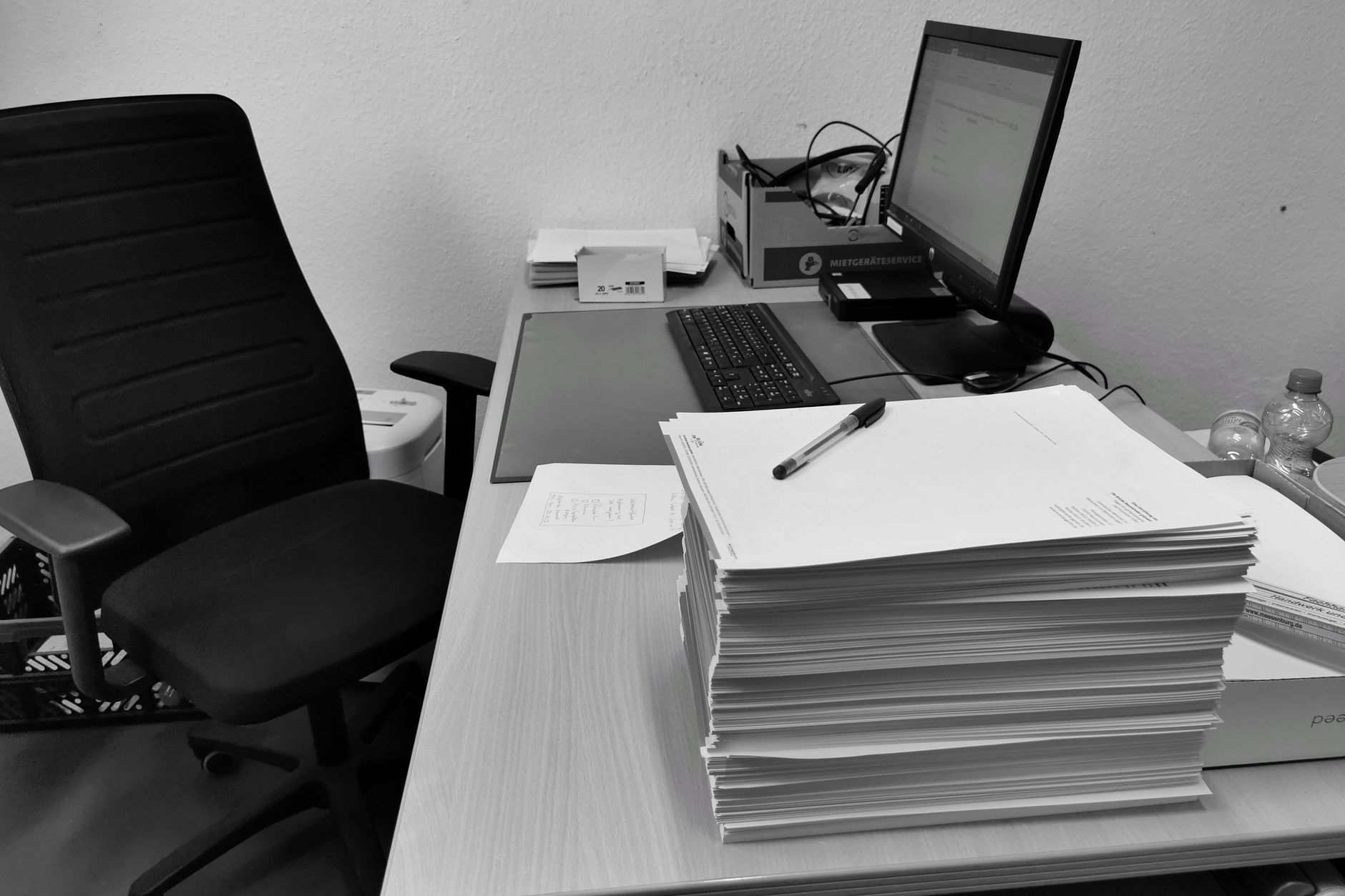 Stacks of paper documents piled high on a desk, more than one person could read