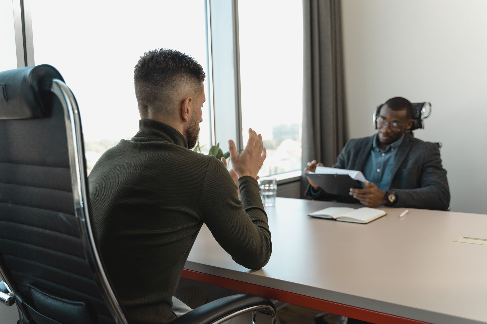 A hiring manager gesturing while explaining something during a video interview, laptop open on a plain desk