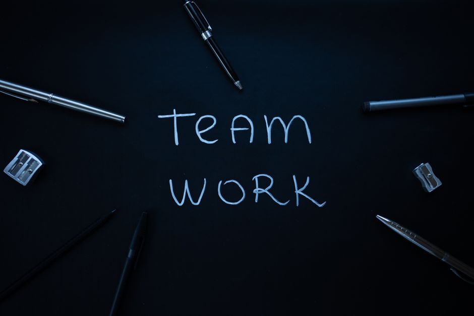 Office supplies arranged around the word teamwork on a dark surface.