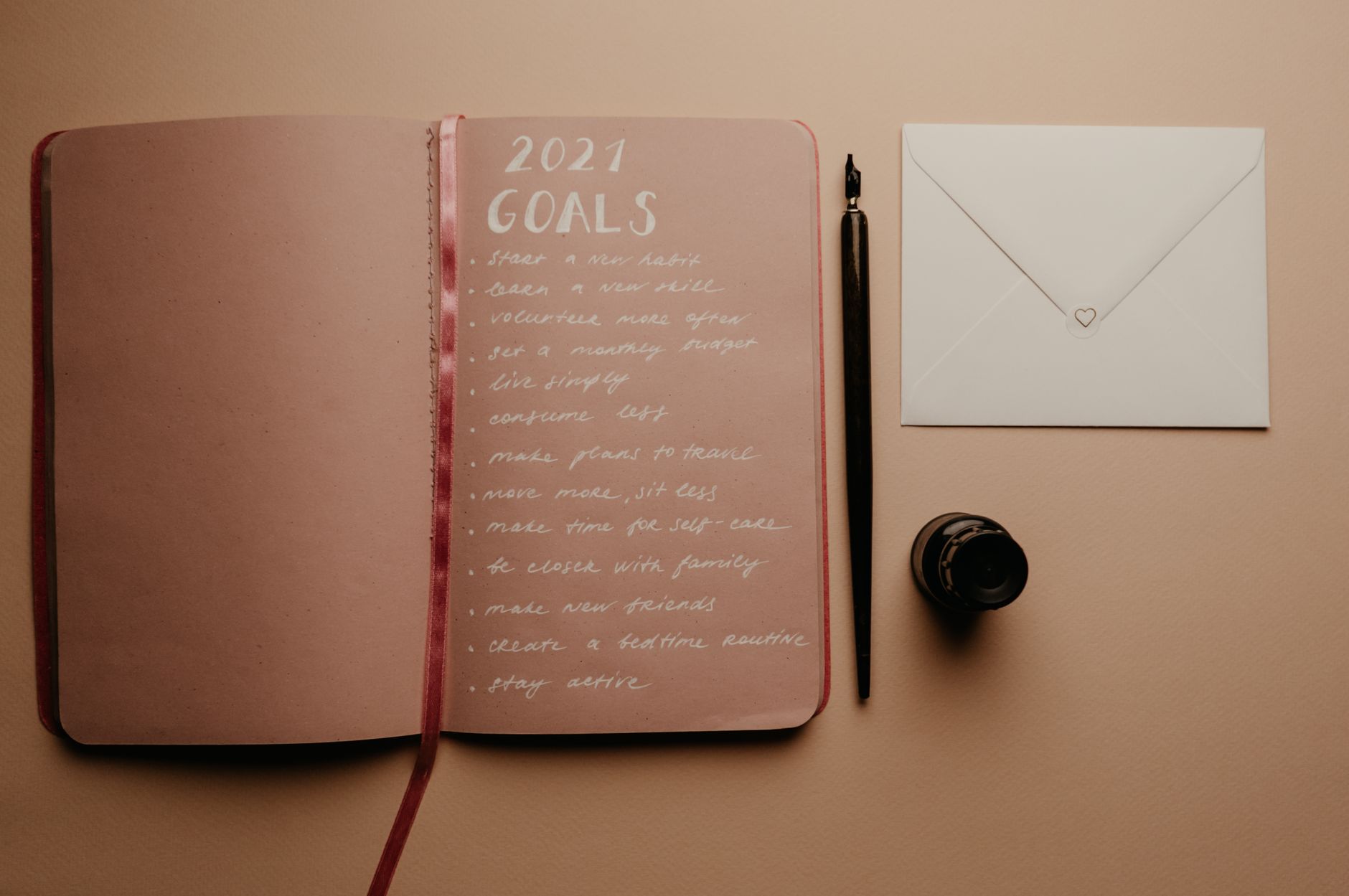 An open notebook with a handwritten list titled 2021 GOALS running to thirteen items, next to a dip pen, ink bottle, and sealed envelope