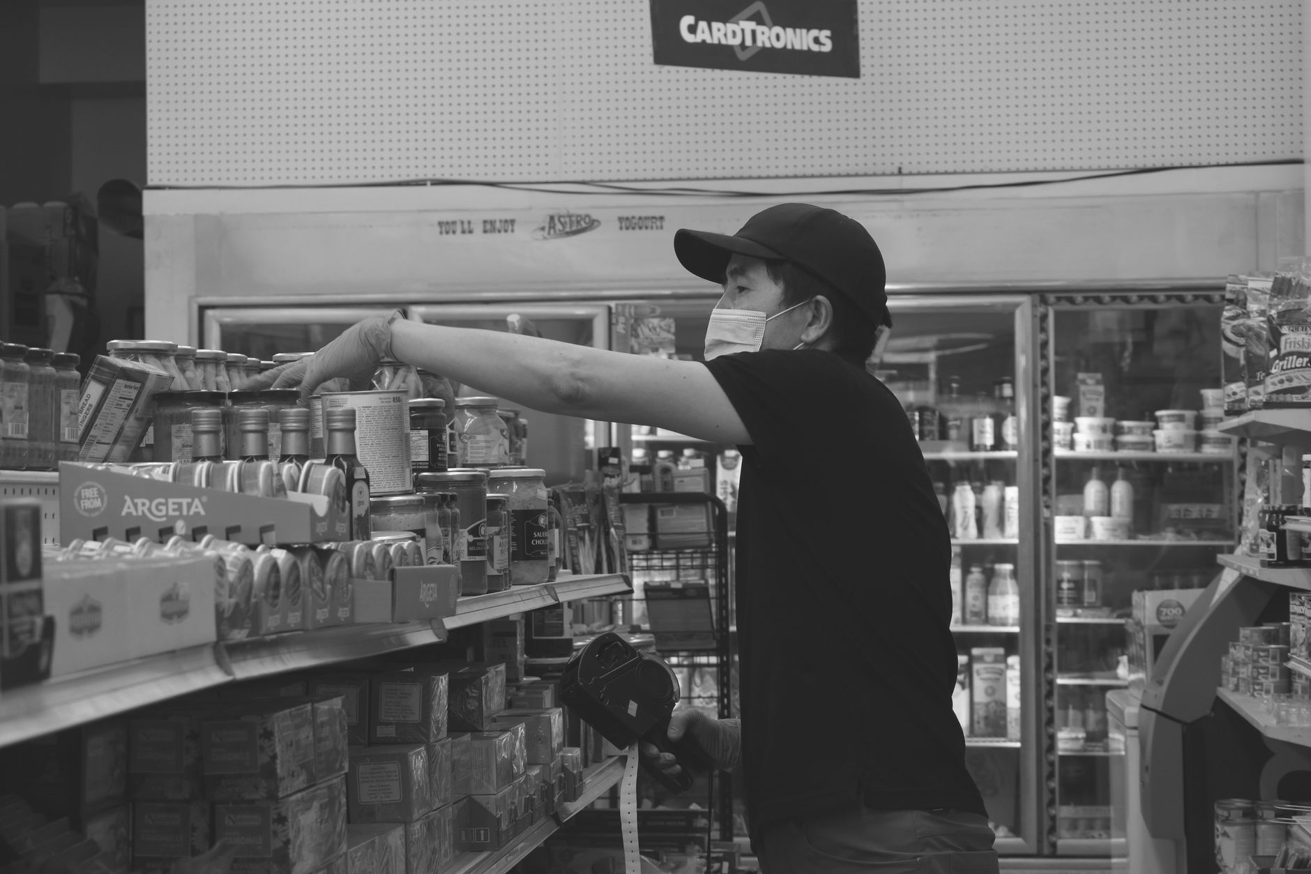 A supermarket aisle with stocked shelves of packaged goods stretching toward the back of the store under bright overhead lighting