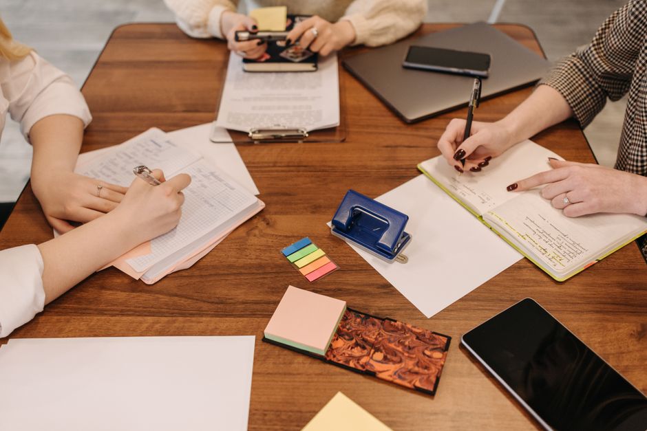 Three colleagues taking notes and reviewing documents during a meeting.
