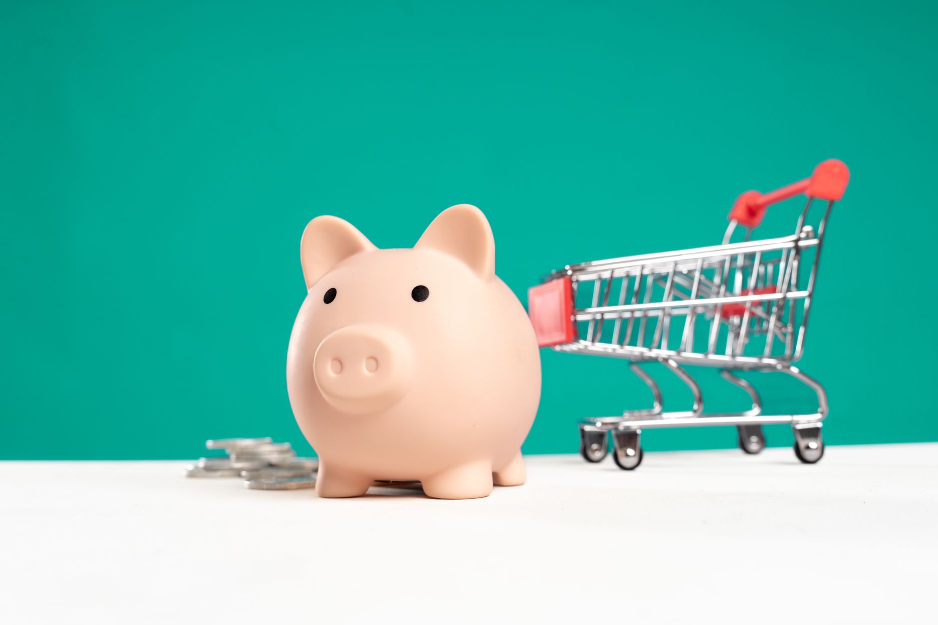 A piggy bank beside a small shopping cart and coins