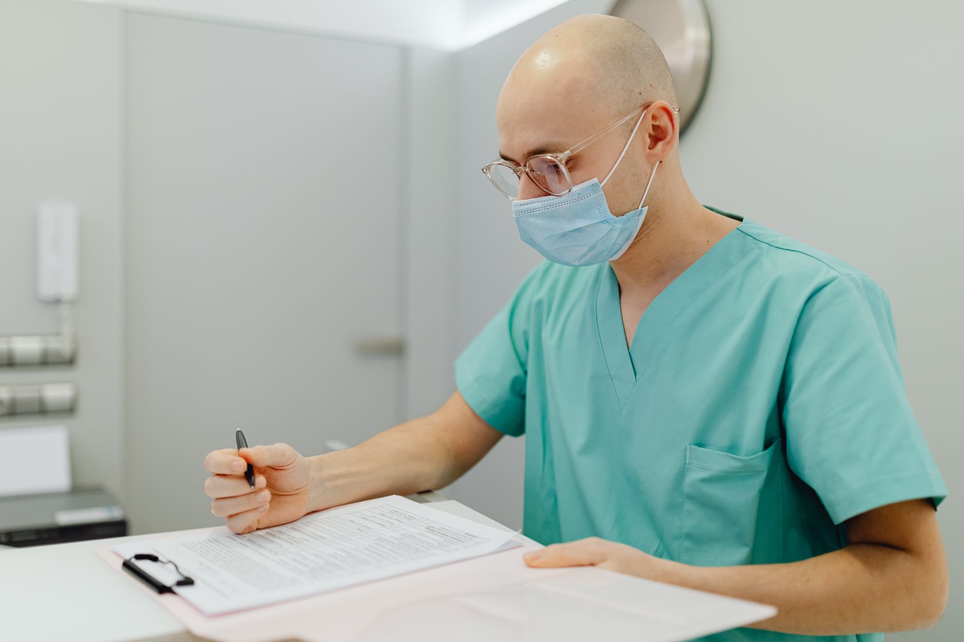 A clinician's hands wrapping a blood pressure cuff around a seated patient's upper arm in a bright exam room