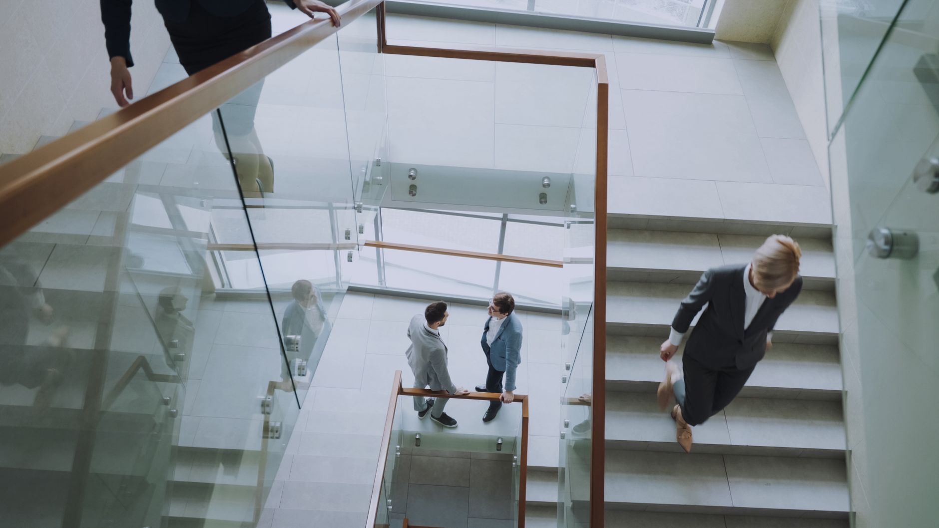 Aerial view of professionals conversing in a glass staircase in a modern office.