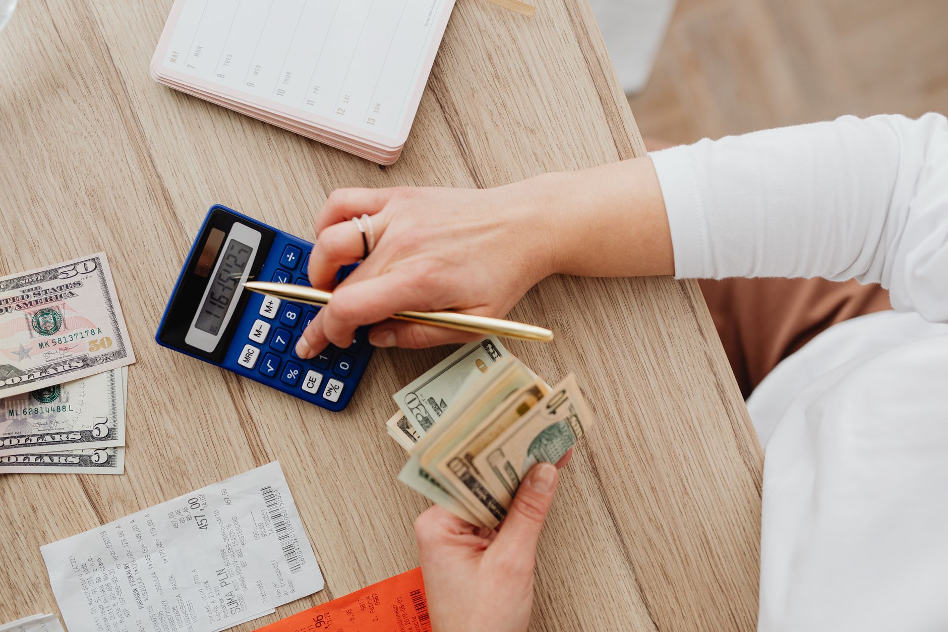 A person counting cash beside receipts and a calculator.