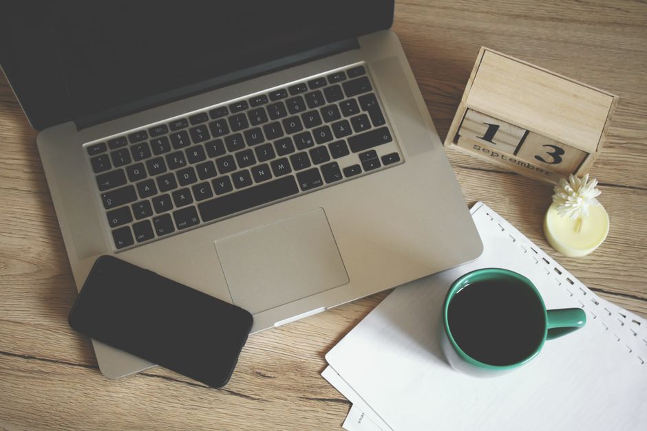 A laptop, coffee, phone, and calendar on a desk.