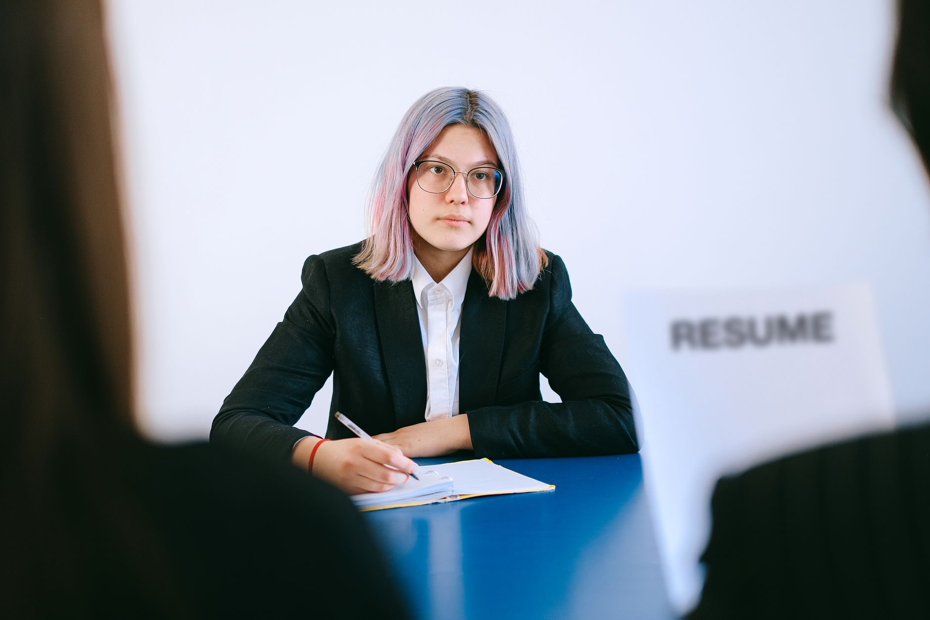 A candidate holding a notebook and pen while listening to two interviewers seated opposite
