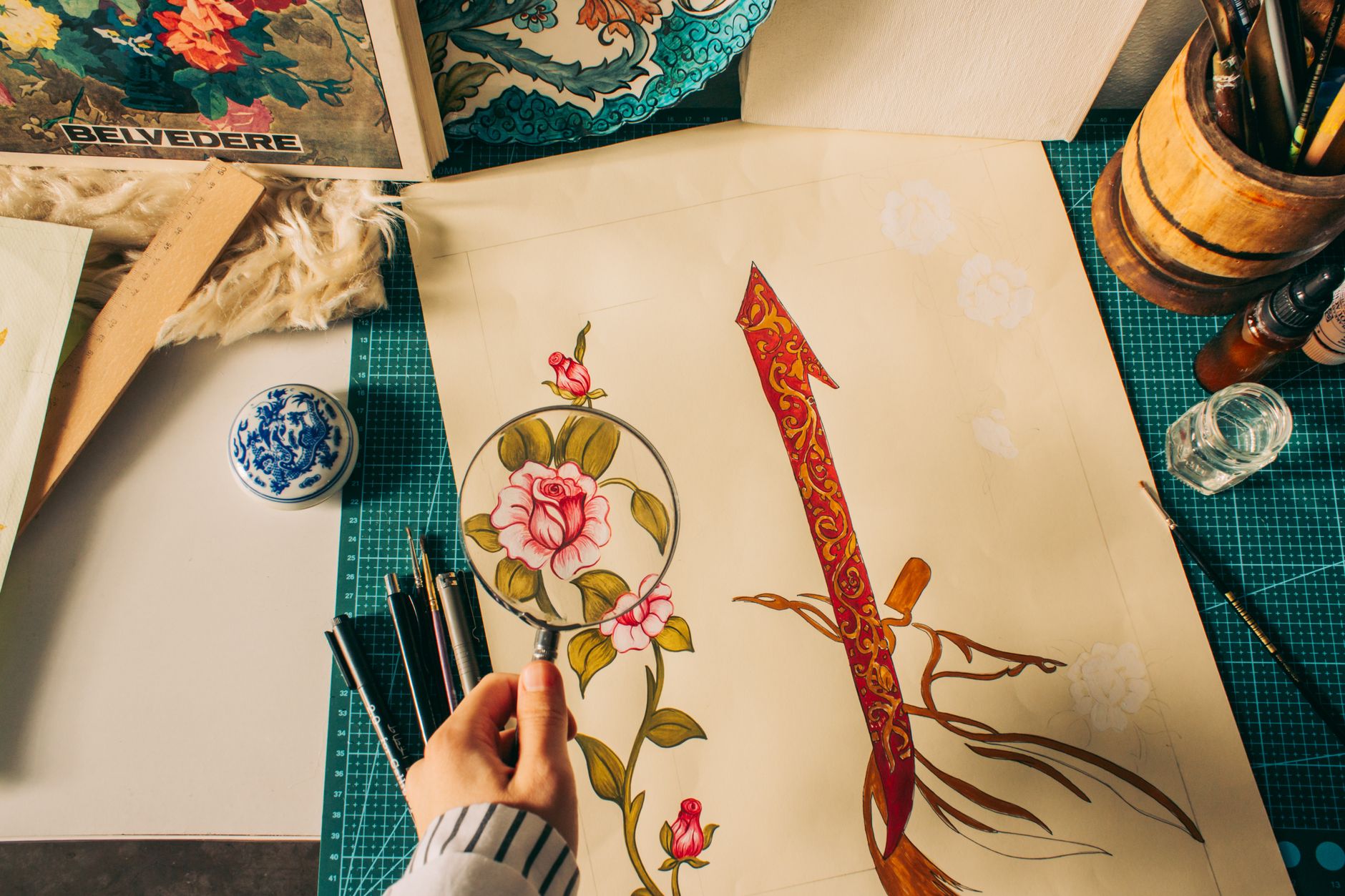 Detailed creative work and tools spread across a desk.