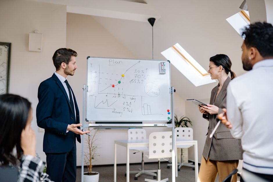 Colleagues discussing charts on a whiteboard during a meeting.