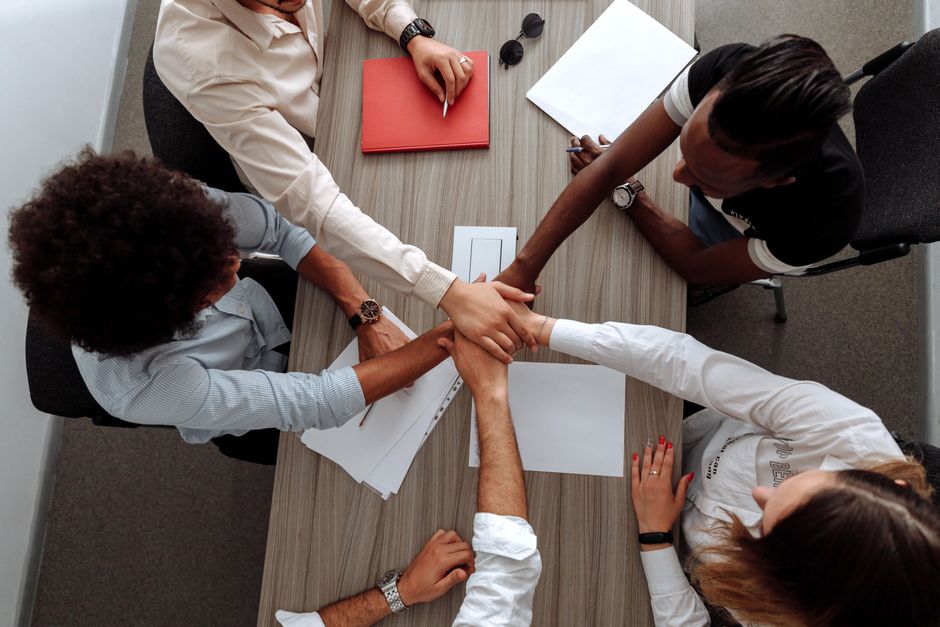 Colleagues placing their hands together over a meeting table.