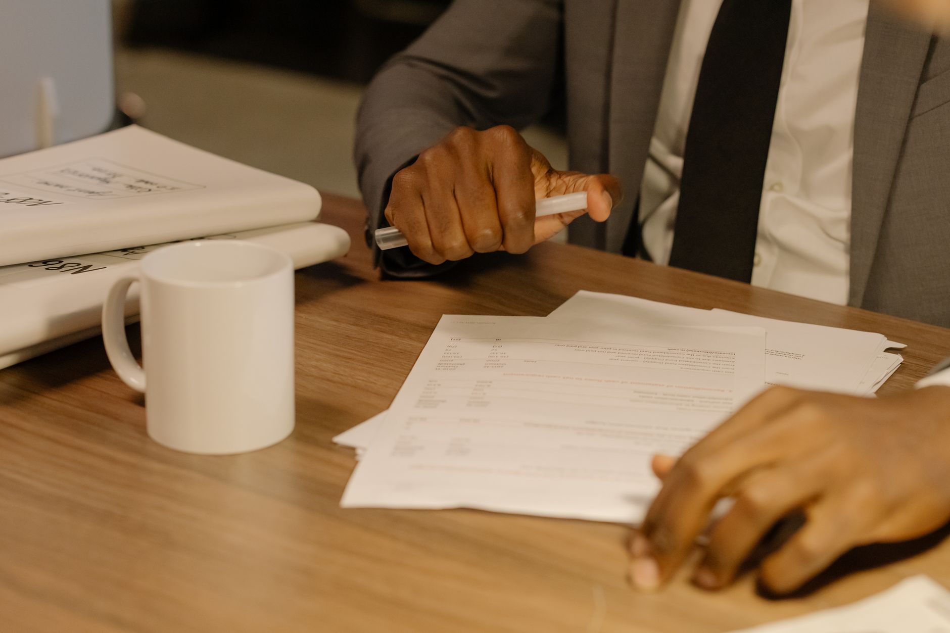 A hiring manager in a suit holds a pen over a stack of printed documents spread across a desk