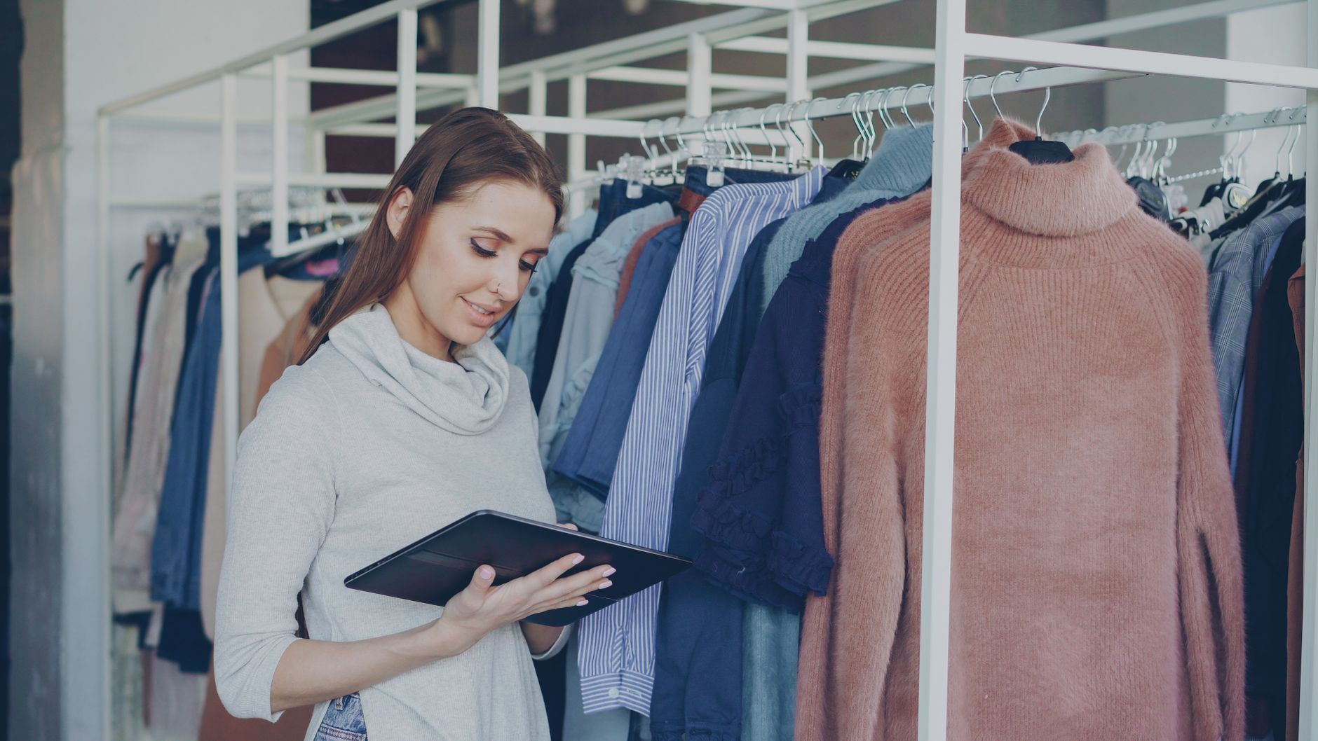 Two retail staff members talking beside a clothing rail in a bright store, one holding a tablet