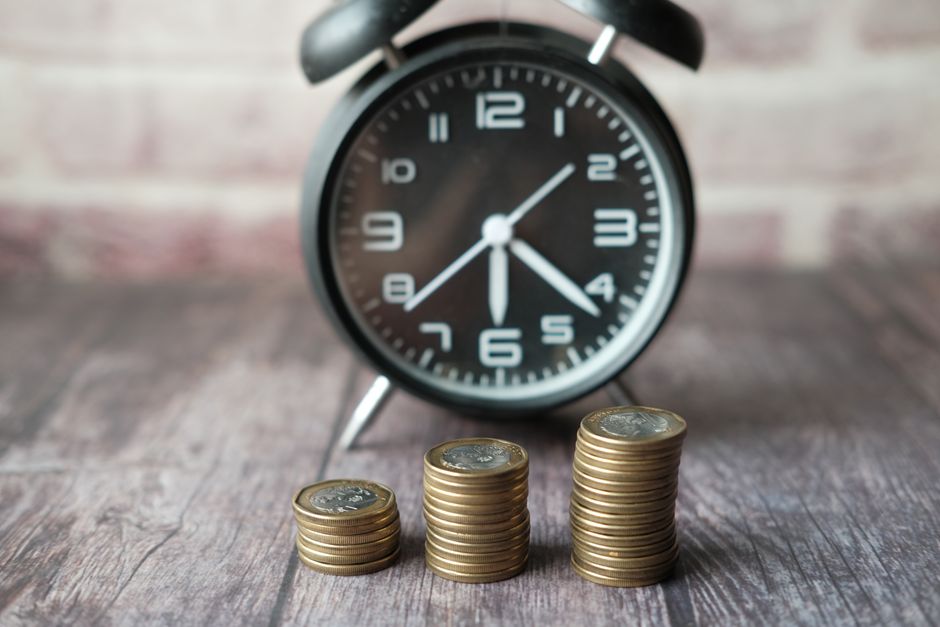 Stacks of coins beside a clock illustrate the relationship between time and compounding.