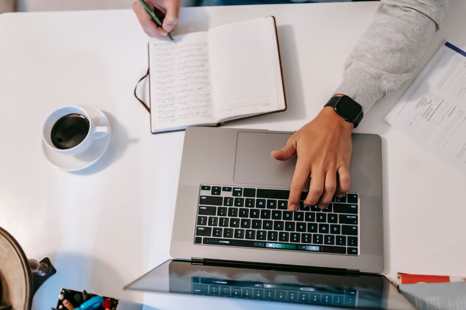 A person using a laptop and writing notes in a notebook.