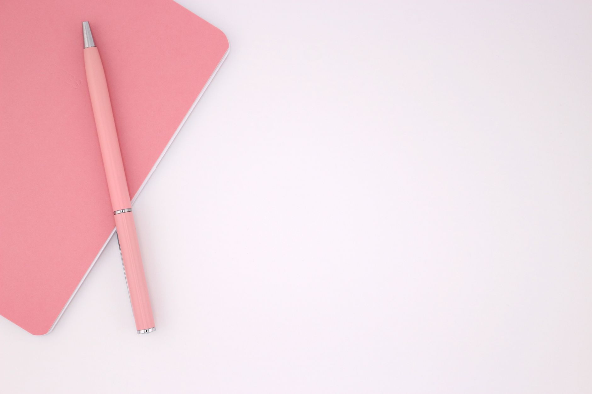 A single open notebook and one pen on a bare wooden desk, with everything else pushed out of frame