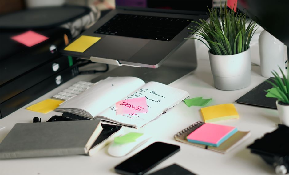 A working desk with a laptop, checklists, and sticky notes.