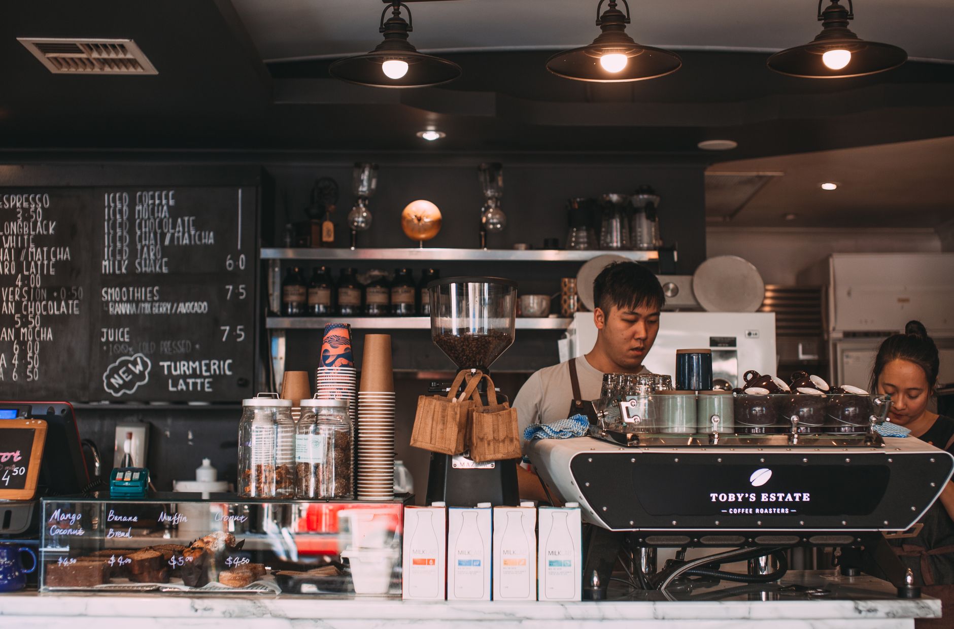 A Starbucks barista smiling while handing a drink across the counter to a customer