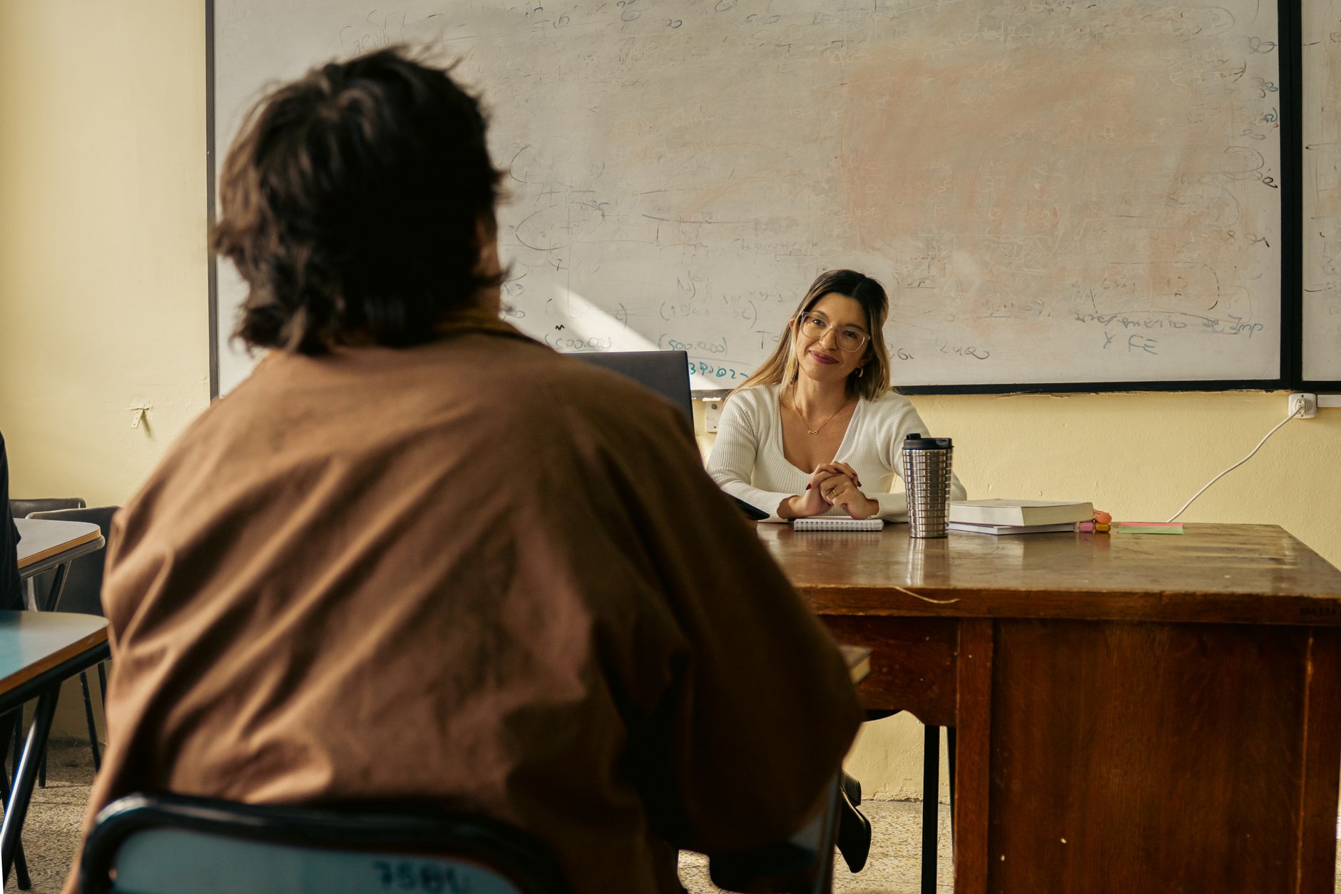A teacher kneeling beside a student's desk, pointing at their notebook during independent work time