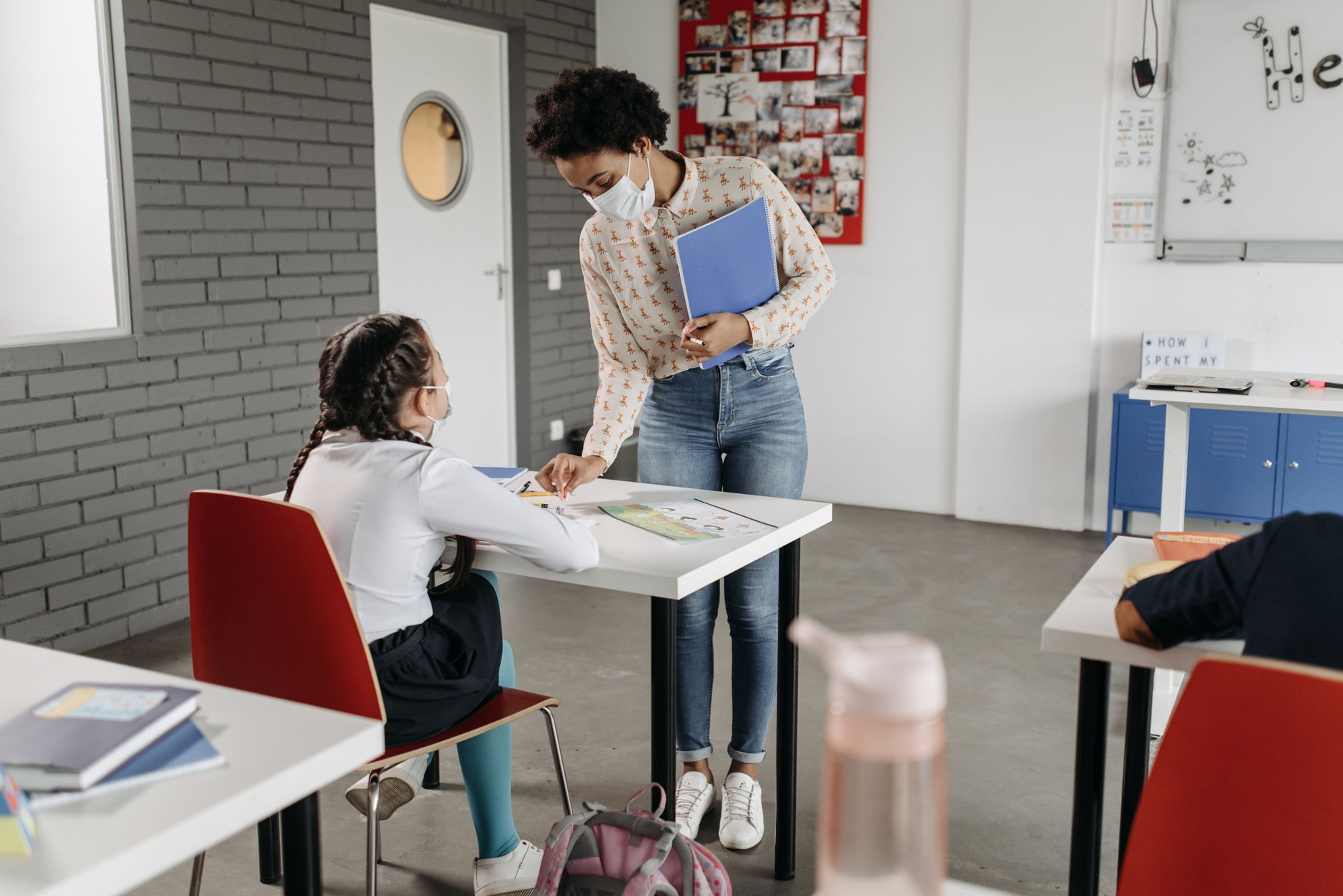 A small group of students working together at a table while a teacher observes and takes notes