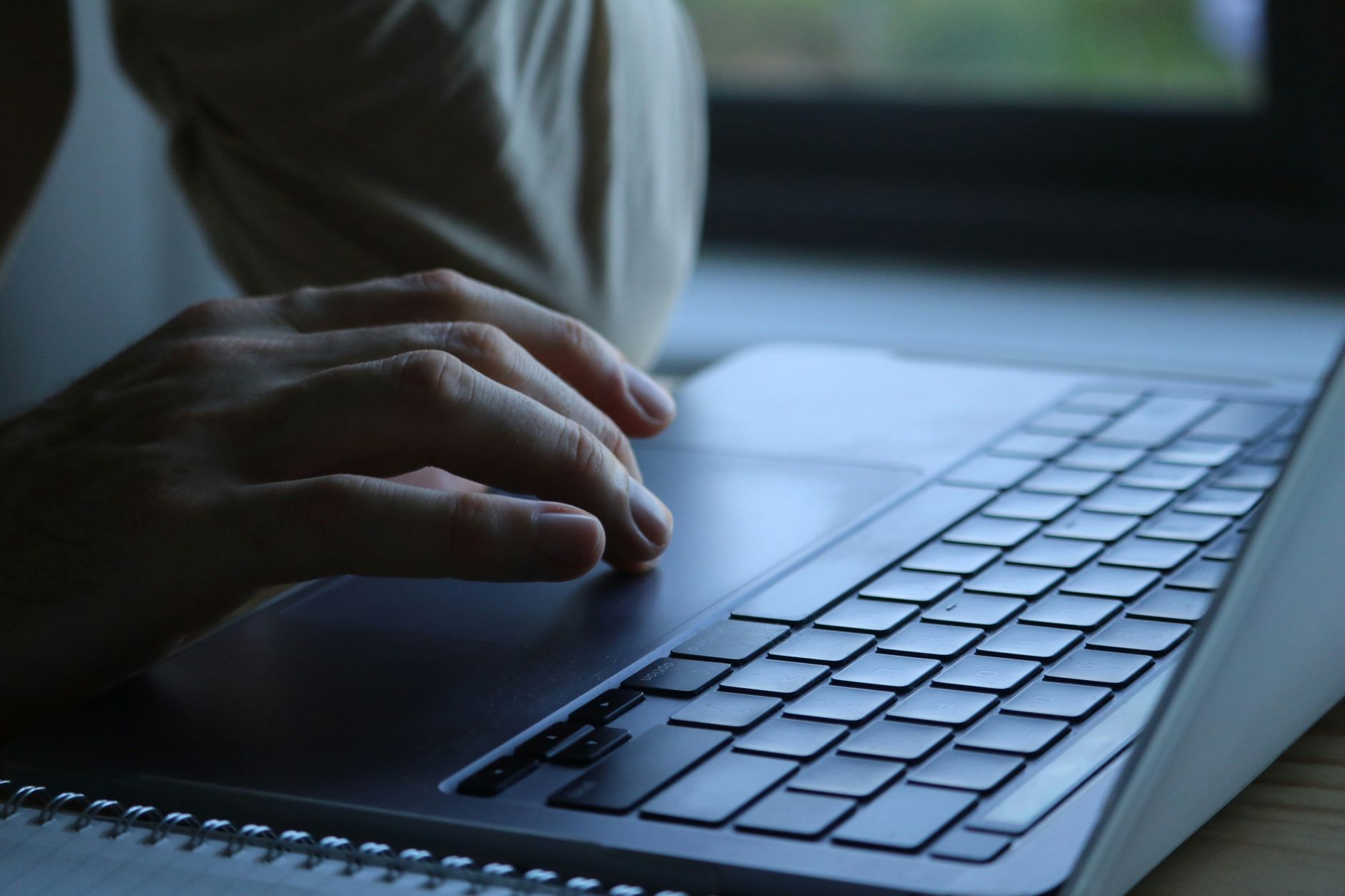 Close-up of hands typing an email on a laptop keyboard at a small desk