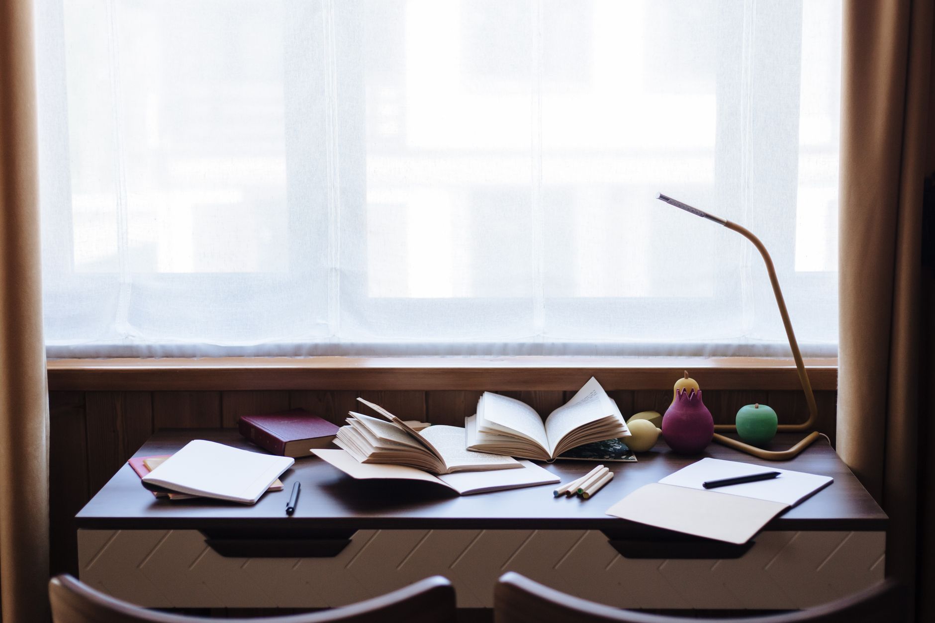 A person sitting on a bed early in the morning, writing in a notebook beside an open laptop