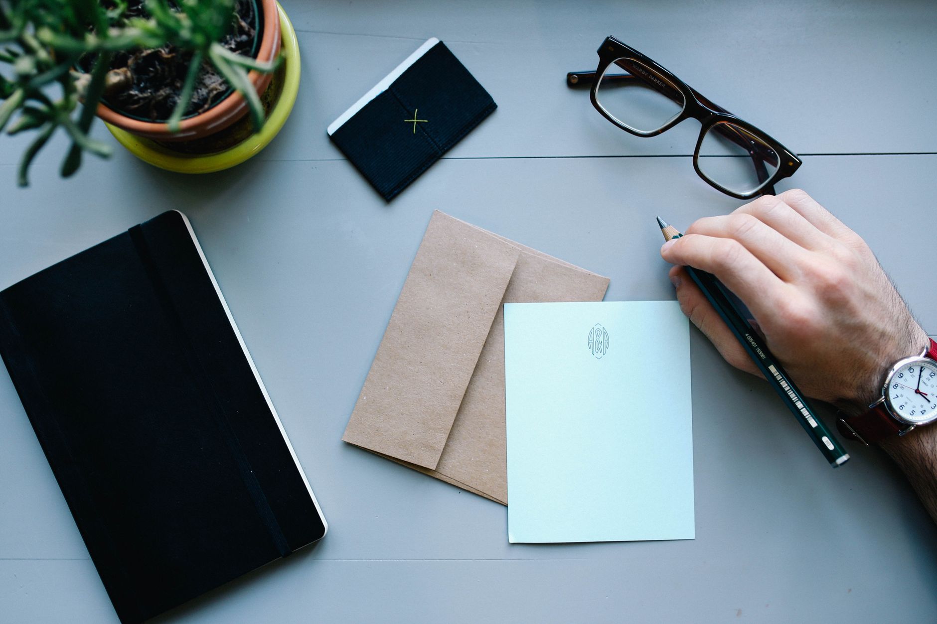 Desk with an envelope, notebook, glasses, and writing tools